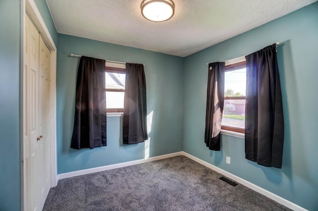 carpeted empty room with a textured ceiling, visible vents, and baseboards