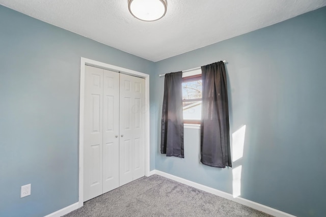 unfurnished bedroom featuring a textured ceiling, carpet floors, a closet, and baseboards