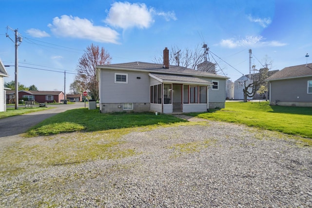 back of house featuring a sunroom, gravel driveway, a chimney, and a lawn