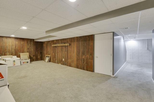 finished basement featuring wooden walls, visible vents, carpet floors, and a drop ceiling