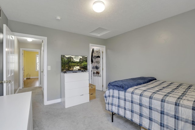bedroom with attic access, baseboards, a textured ceiling, and light colored carpet