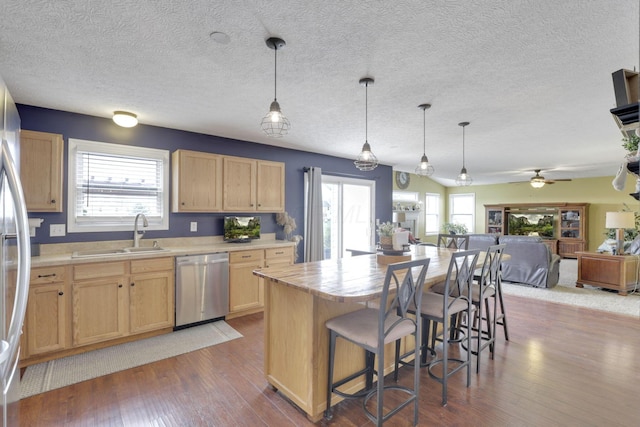 kitchen featuring light brown cabinets, stainless steel dishwasher, open floor plan, and a sink
