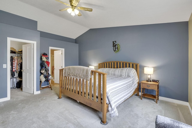 carpeted bedroom with vaulted ceiling, a spacious closet, a ceiling fan, and baseboards