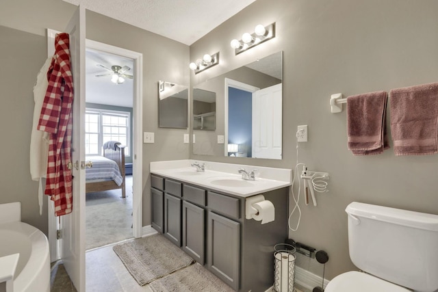 ensuite bathroom featuring toilet, a sink, double vanity, and baseboards