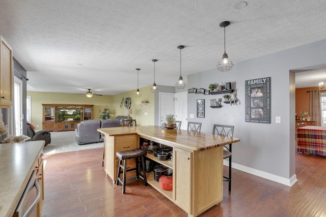 kitchen with a breakfast bar, a kitchen island, dark wood-style flooring, baseboards, and ceiling fan
