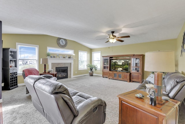 living room with vaulted ceiling, ceiling fan, carpet floors, a tiled fireplace, and baseboards