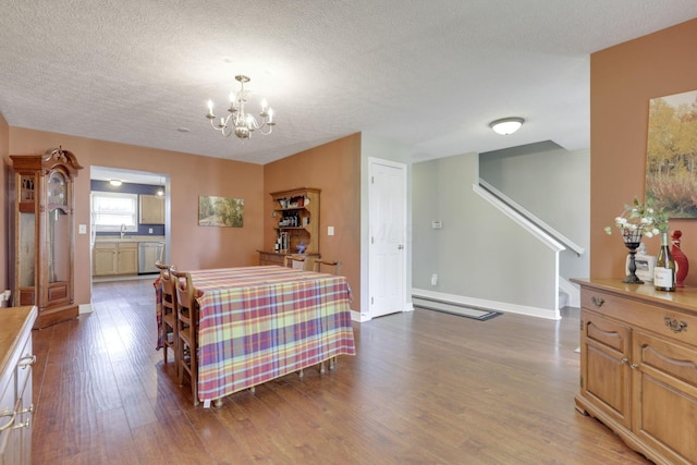 dining room with wood finished floors, a textured ceiling, a baseboard heating unit, an inviting chandelier, and baseboards