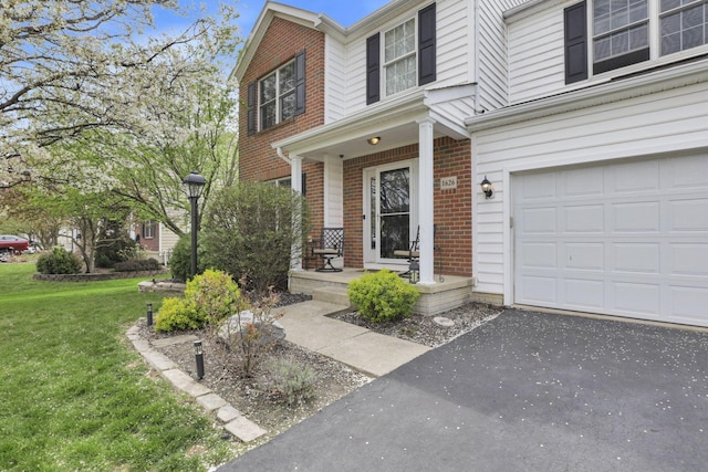 view of exterior entry featuring aphalt driveway, a porch, a lawn, brick siding, and a garage