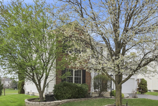 view of property hidden behind natural elements featuring brick siding, driveway, a front yard, and a garage