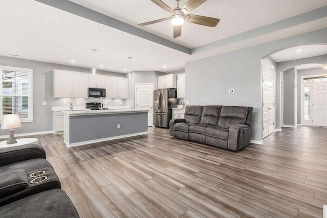 living room featuring a ceiling fan, arched walkways, a healthy amount of sunlight, and baseboards