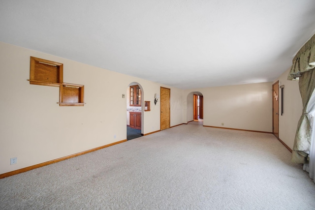 spare room with arched walkways, baseboards, and light colored carpet