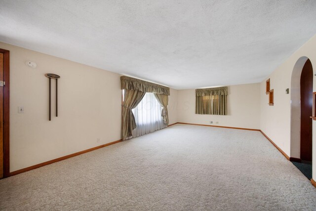 carpeted empty room with arched walkways, baseboards, and a textured ceiling