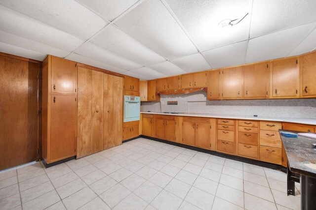 kitchen with light countertops, brown cabinetry, a drop ceiling, and oven