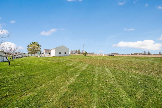 view of yard featuring a rural view, an outbuilding, and fence