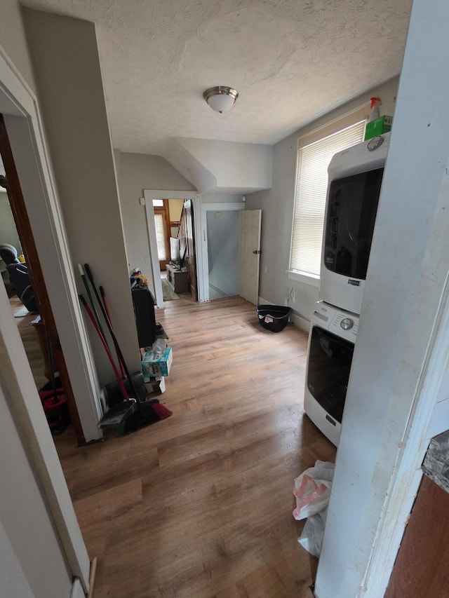 corridor featuring estacked washer and dryer, wood finished floors, and a textured ceiling