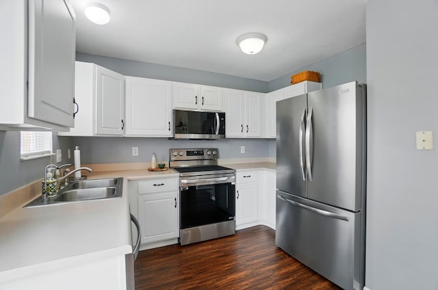 kitchen with dark wood-style flooring, appliances with stainless steel finishes, a sink, light countertops, and white cabinetry