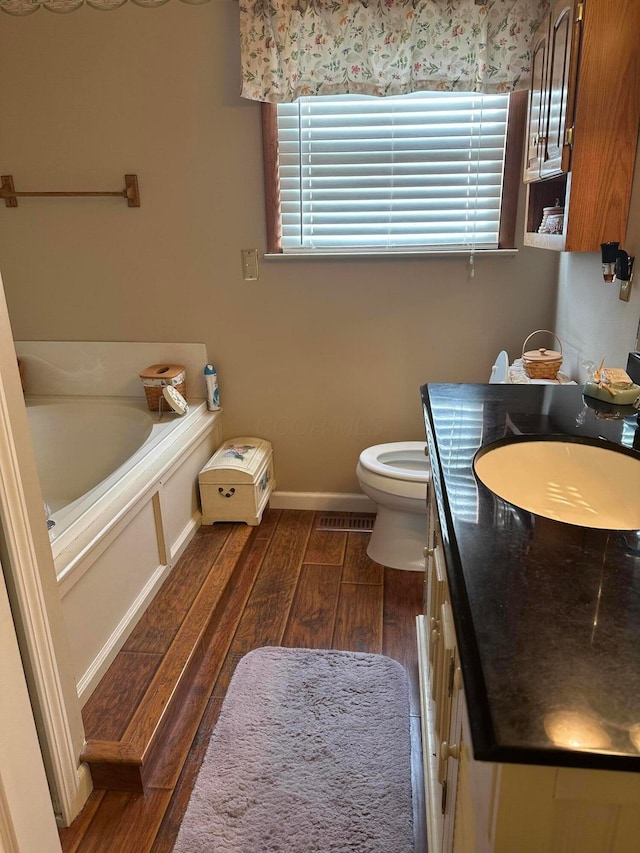 bathroom with wood finished floors, toilet, vanity, a bath, and baseboards