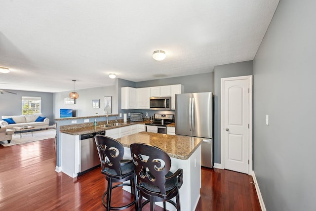 kitchen with a sink, dark wood-style flooring, appliances with stainless steel finishes, and a peninsula