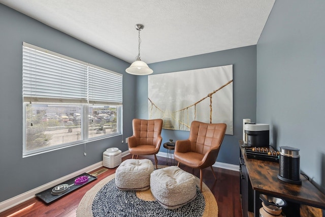 living area with baseboards, a textured ceiling, and wood finished floors