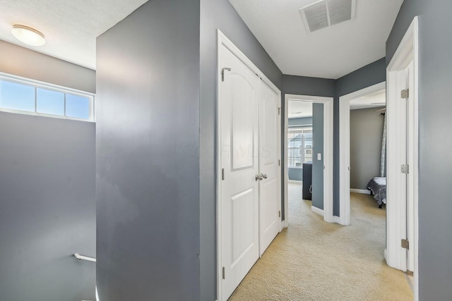 hall with a healthy amount of sunlight, baseboards, light carpet, and visible vents