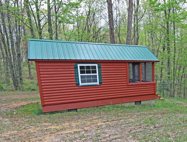 view of side of property featuring metal roof, log veneer siding, and a view of trees
