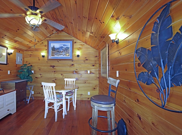 dining area with wood walls, hardwood / wood-style flooring, a ceiling fan, and vaulted ceiling