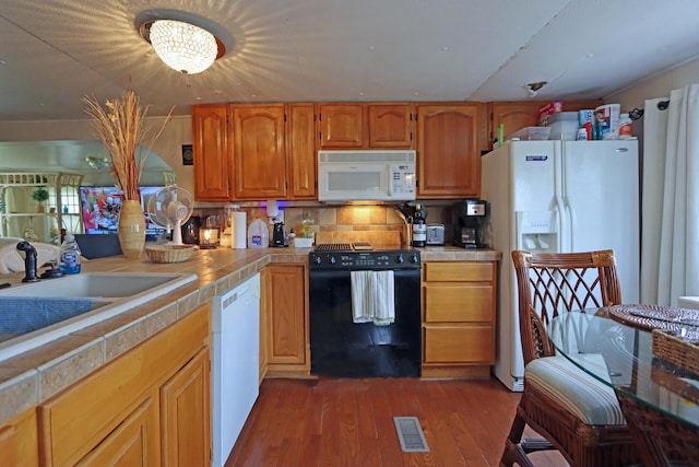 kitchen featuring a sink, tile counters, dark wood-style flooring, visible vents, and white appliances