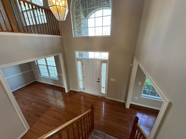 foyer entrance with baseboards, plenty of natural light, wood finished floors, and a towering ceiling