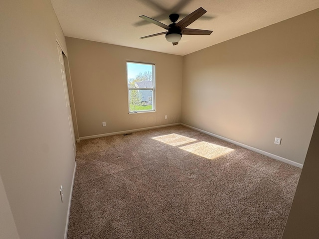 carpeted spare room with baseboards, a ceiling fan, and visible vents