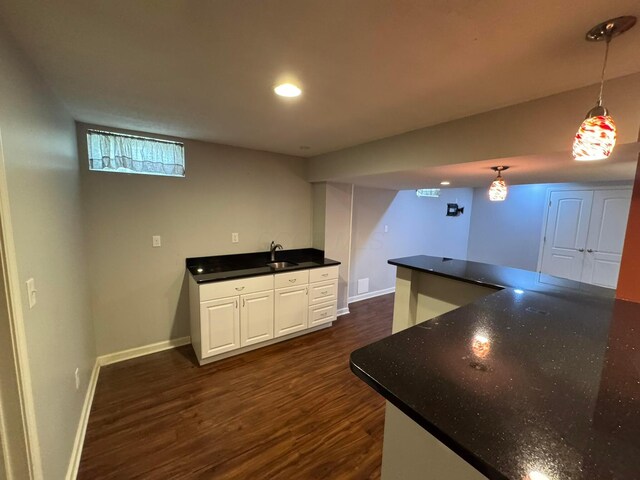 kitchen with a sink, white cabinetry, decorative light fixtures, baseboards, and dark wood-style floors
