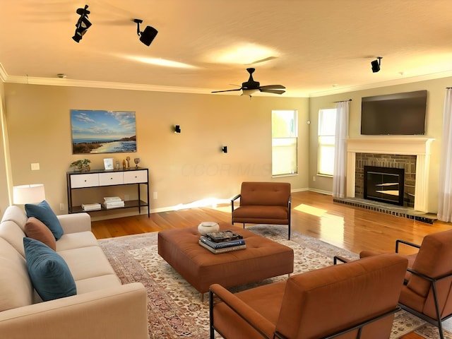 living room with a ceiling fan, crown molding, wood finished floors, baseboards, and a glass covered fireplace