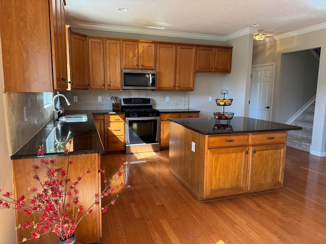 kitchen featuring brown cabinetry, crown molding, wood finished floors, a sink, and appliances with stainless steel finishes