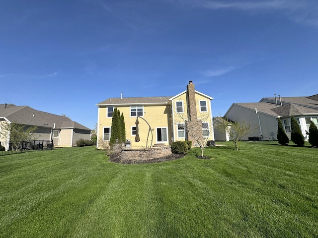 rear view of house with fence, a chimney, and a yard