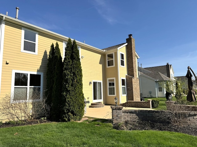 rear view of property with a lawn, a chimney, and a patio area