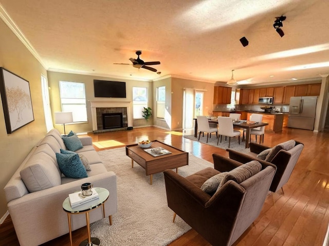 living room featuring a ceiling fan, hardwood / wood-style flooring, a tile fireplace, baseboards, and ornamental molding
