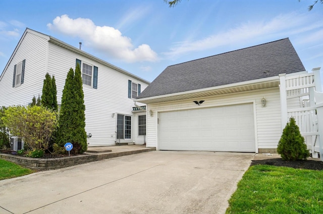 view of front facade featuring an attached garage, driveway, roof with shingles, and central AC