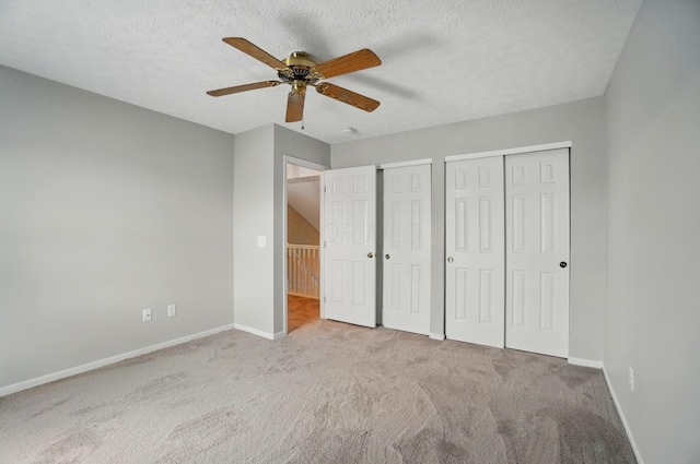 unfurnished bedroom featuring carpet floors, multiple closets, a textured ceiling, and baseboards