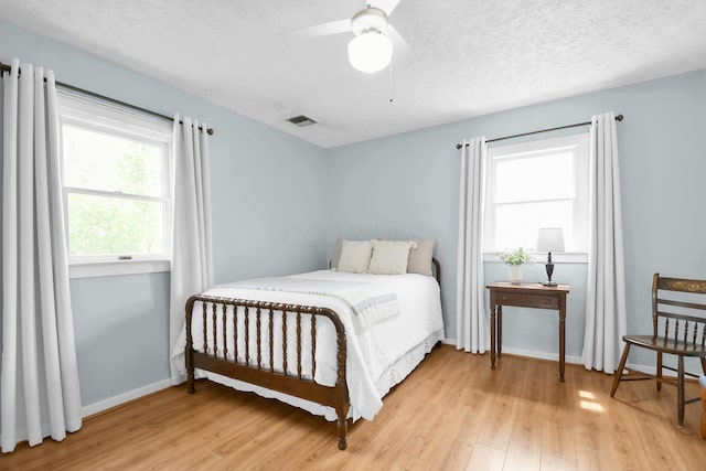 bedroom with a textured ceiling, baseboards, visible vents, and light wood-style flooring