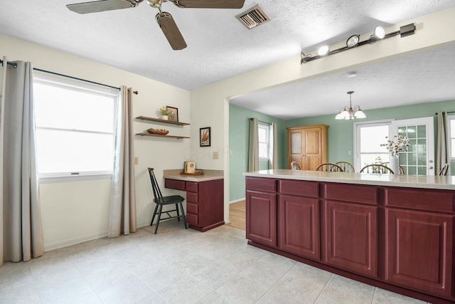 kitchen with light countertops, dark brown cabinets, visible vents, and ceiling fan with notable chandelier