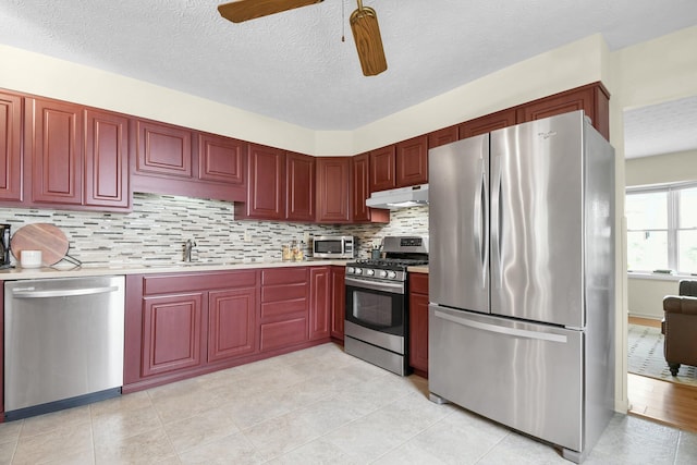 kitchen with reddish brown cabinets, a sink, under cabinet range hood, and stainless steel appliances
