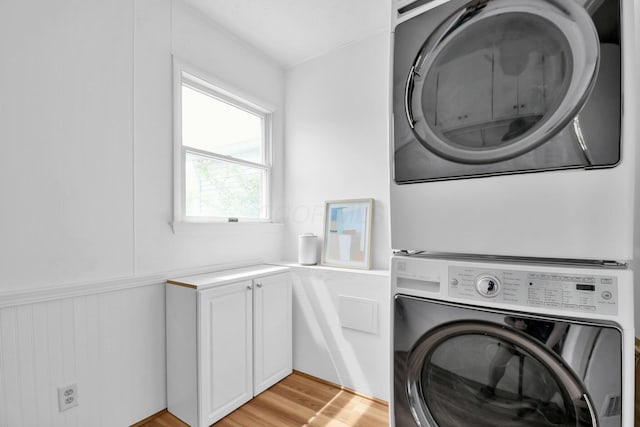 washroom with cabinet space, stacked washing maching and dryer, and light wood-type flooring