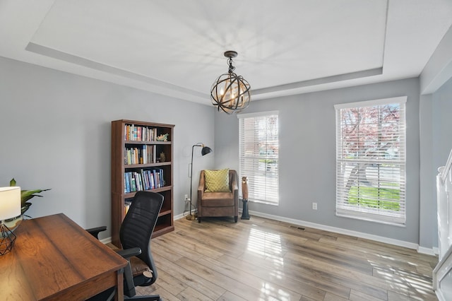 home office with a tray ceiling, light wood-style floors, baseboards, and a notable chandelier