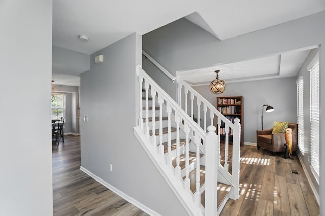 staircase featuring wood finished floors, a chandelier, a tray ceiling, baseboards, and visible vents