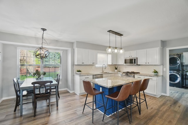 kitchen with stacked washer / drying machine, a sink, a chandelier, appliances with stainless steel finishes, and white cabinetry