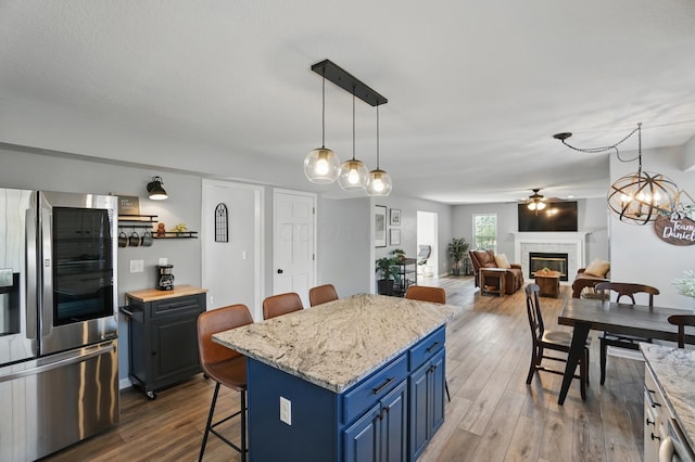 kitchen featuring a ceiling fan, a kitchen breakfast bar, blue cabinets, a glass covered fireplace, and stainless steel fridge