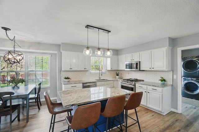 kitchen with light wood-type flooring, appliances with stainless steel finishes, stacked washer / dryer, and a sink