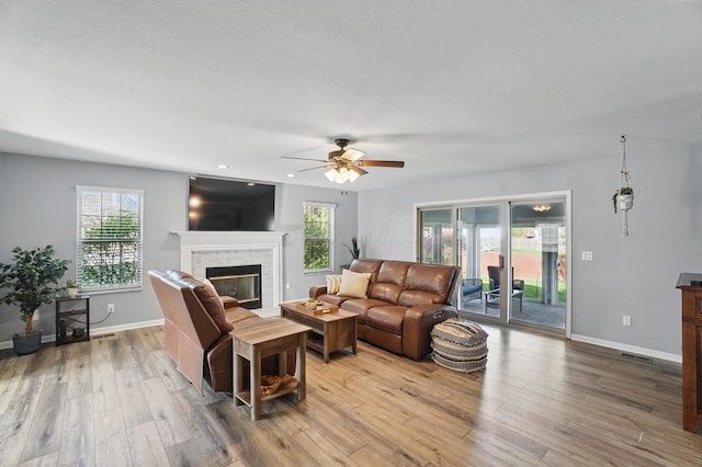 living area featuring a premium fireplace, baseboards, wood finished floors, and ceiling fan