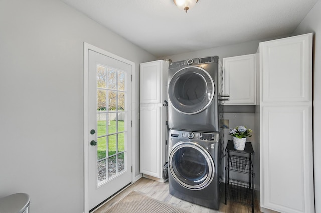 laundry room featuring light wood finished floors, stacked washing maching and dryer, and cabinet space