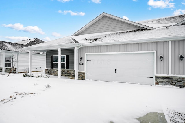 snow covered property featuring stone siding, a porch, and a garage