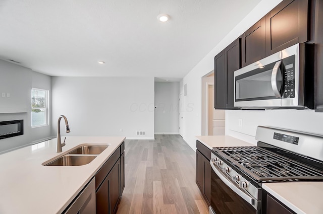 kitchen with stainless steel appliances, light wood-style flooring, a sink, dark brown cabinets, and light countertops